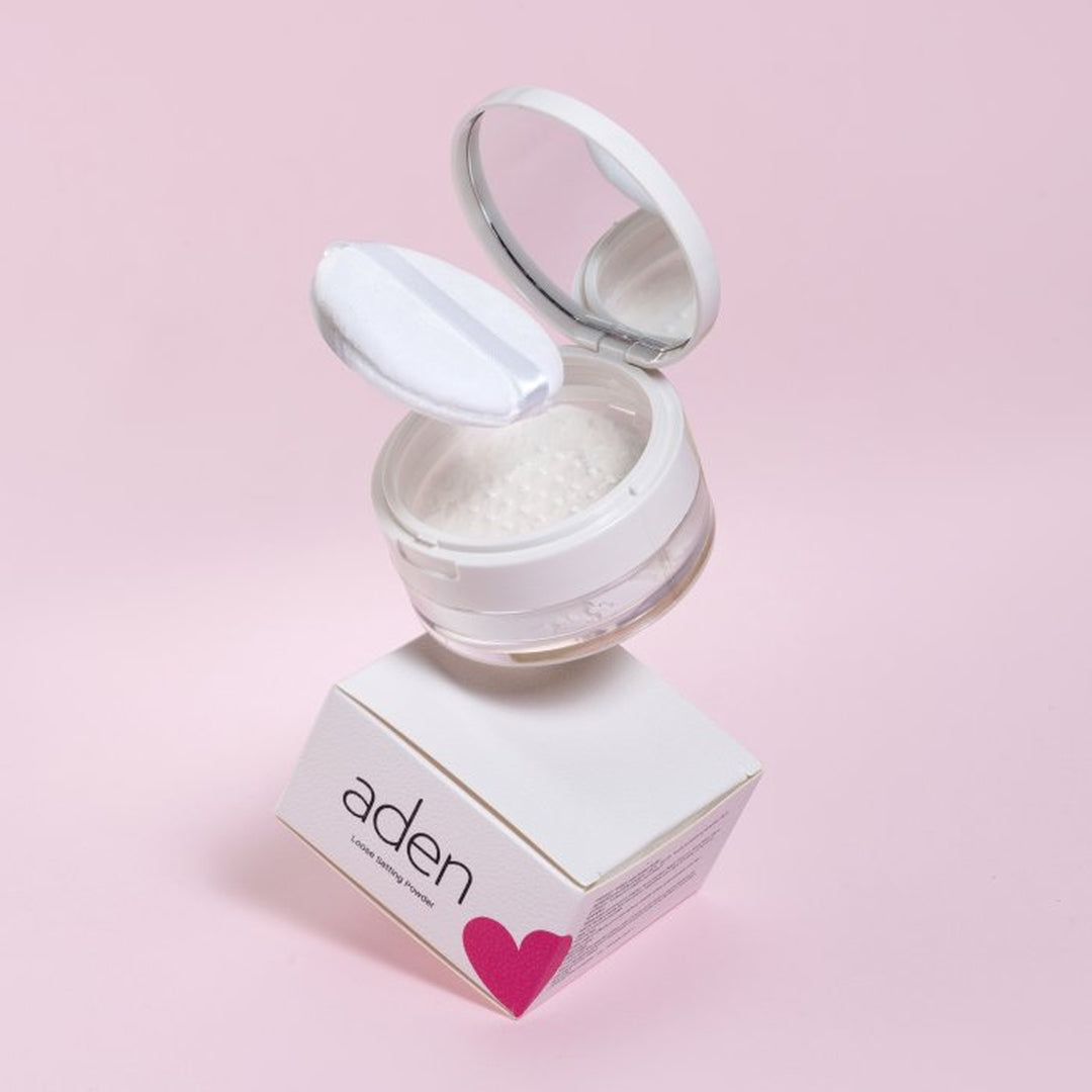 Aden Loose Setting Powder 10g διάφανη λεπτόκοκκη πούδρα σταθεροποίησης μακιγιάζ σε ανοιχτή συσκευασία με καθρέφτη και puff, πάνω σε λευκό κουτί με ροζ λεπτομέρεια, σε ροζ φόντο